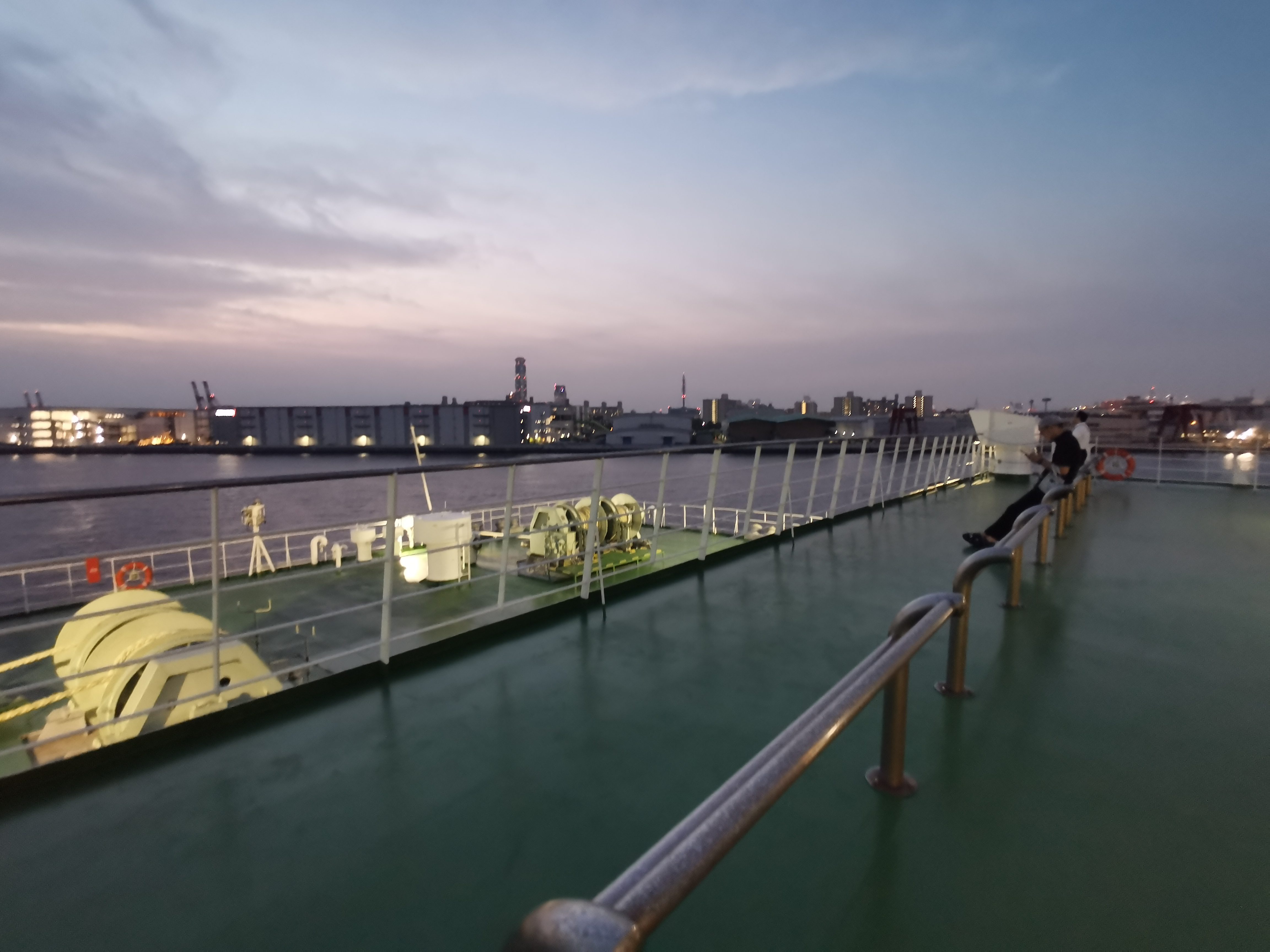 Outdoor ferry deck view at sunset departing Osaka on overnight ferry to Fukuoka Moji with city skyline and water
