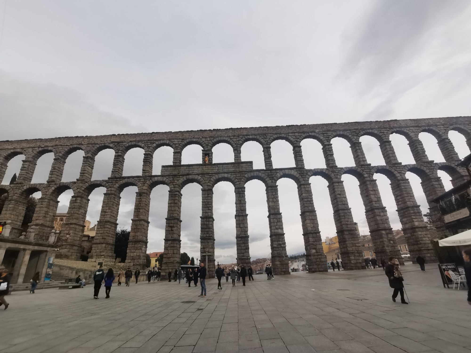 西班牙塞哥维亚大渡槽，高大的罗马石拱桥横跨广场，游客在下方行走